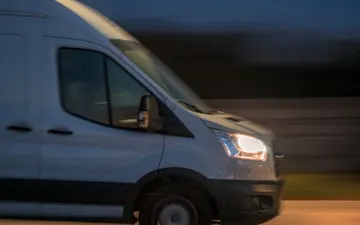 Dubă albă de livrare circulând noaptea, în mișcare